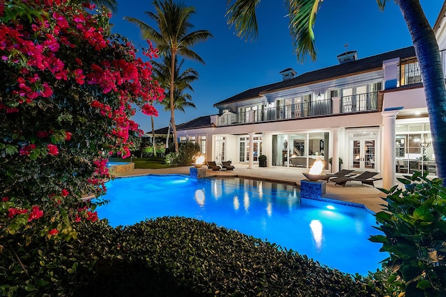 rear view of house with stucco siding, french doors, a balcony, a patio area, and an outdoor pool