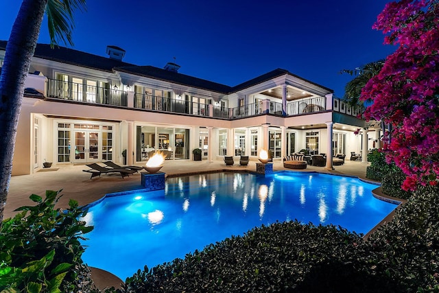 back of house at night with french doors, a patio, a balcony, and stucco siding