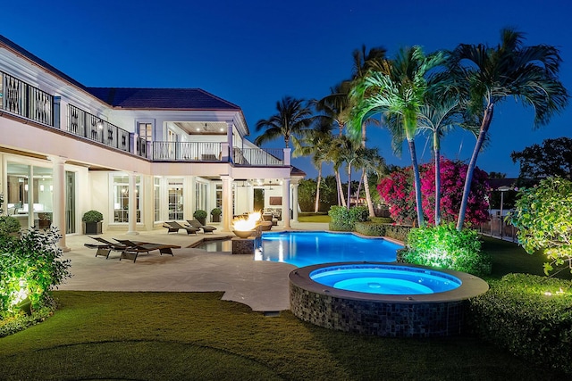 pool at night with a patio area, an outdoor pool, an in ground hot tub, and a yard