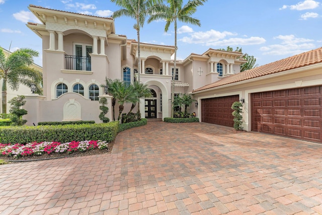 mediterranean / spanish-style home with a balcony, a garage, french doors, decorative driveway, and stucco siding