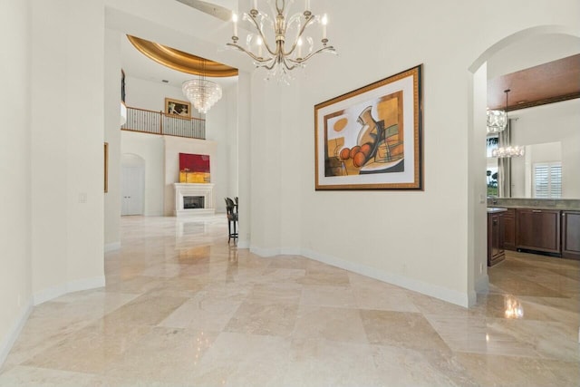 hall featuring arched walkways, marble finish floor, a notable chandelier, and baseboards