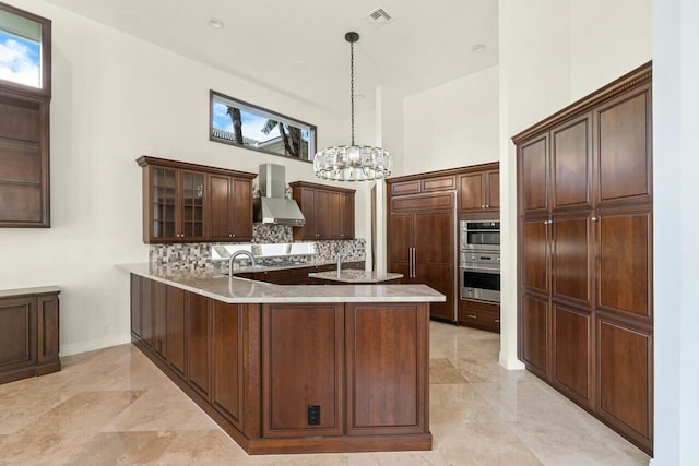 kitchen featuring a peninsula, a high ceiling, visible vents, wall chimney exhaust hood, and tasteful backsplash