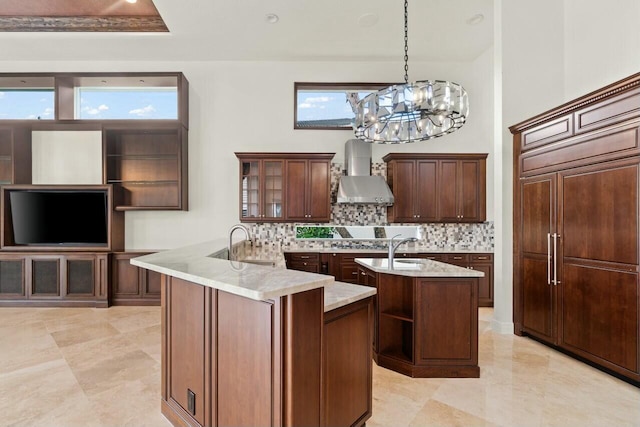 kitchen featuring paneled built in fridge, wall chimney range hood, backsplash, and an island with sink