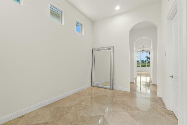 unfurnished room featuring arched walkways, marble finish floor, baseboards, and recessed lighting