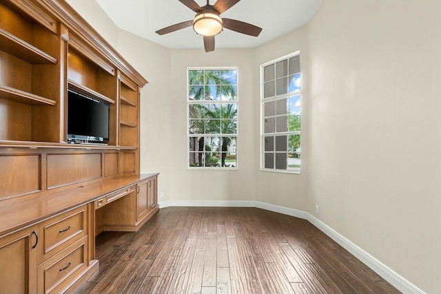 unfurnished office featuring a ceiling fan, built in study area, dark wood finished floors, and baseboards