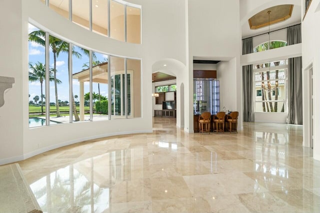 entryway featuring arched walkways, marble finish floor, a high ceiling, and baseboards