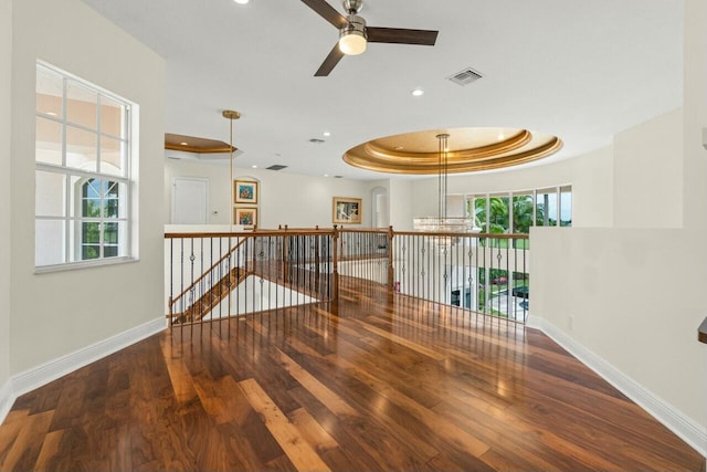 empty room featuring a raised ceiling, visible vents, baseboards, and wood finished floors