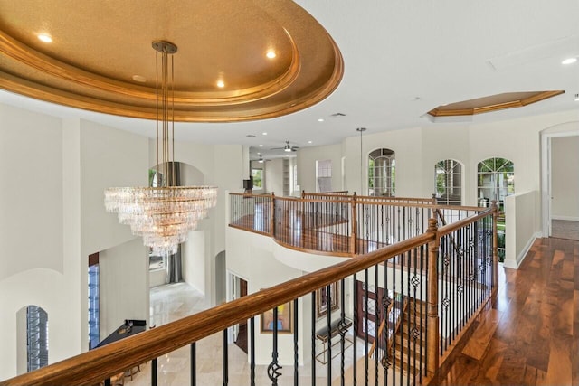 corridor featuring a tray ceiling, recessed lighting, an inviting chandelier, an upstairs landing, and wood finished floors