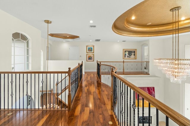 corridor with recessed lighting, a raised ceiling, visible vents, an upstairs landing, and wood finished floors