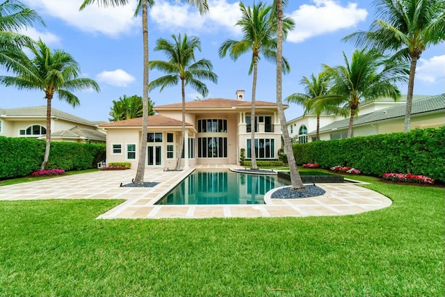 rear view of house with stucco siding, a fenced in pool, a lawn, and a patio