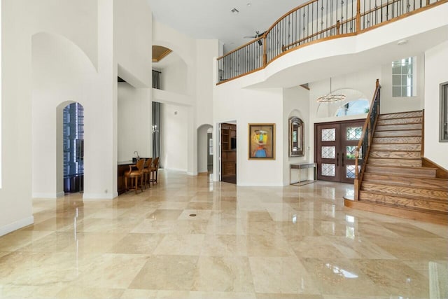 entrance foyer featuring arched walkways, marble finish floor, french doors, baseboards, and stairs