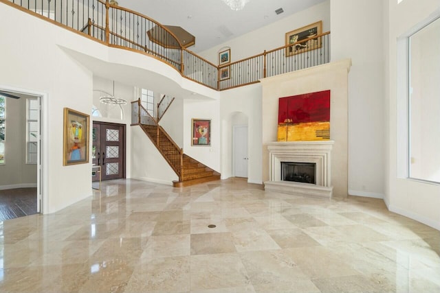 unfurnished living room featuring marble finish floor, a fireplace with raised hearth, a towering ceiling, baseboards, and stairs