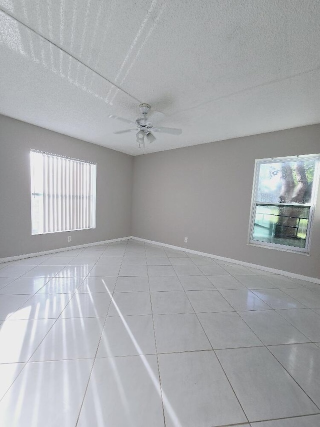 empty room with a ceiling fan, a textured ceiling, baseboards, and light tile patterned floors