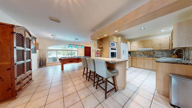 kitchen with light tile patterned flooring, white appliances, a sink, a kitchen island, and backsplash