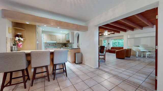 kitchen featuring decorative backsplash, a kitchen breakfast bar, a peninsula, light countertops, and light tile patterned flooring