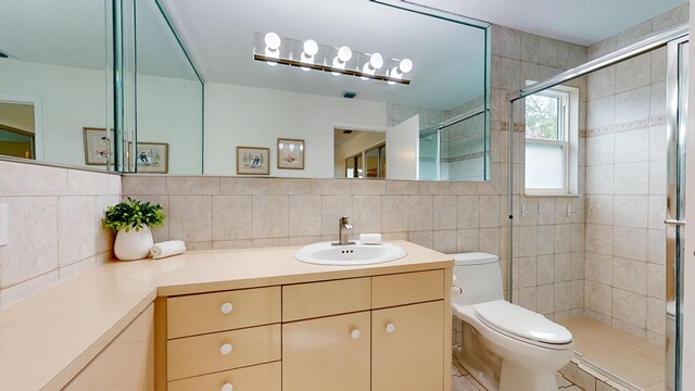 bathroom with tile walls, toilet, a shower stall, vanity, and tile patterned floors