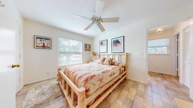 bedroom featuring light wood-style floors, multiple windows, baseboards, and a ceiling fan