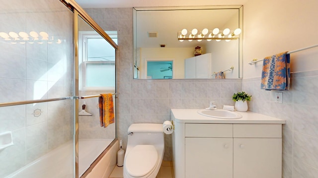 full bath with visible vents, bath / shower combo with glass door, tile walls, and vanity