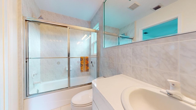 bathroom featuring visible vents, shower / bath combination with glass door, tile walls, and toilet