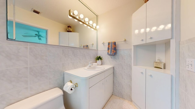 bathroom with tile walls, visible vents, vanity, and toilet