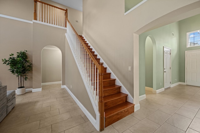 stairway featuring arched walkways, a high ceiling, tile patterned flooring, and baseboards