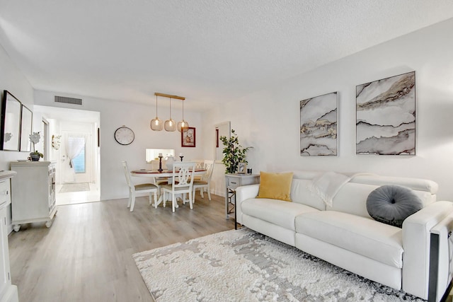 living area with a textured ceiling, light wood-type flooring, and visible vents