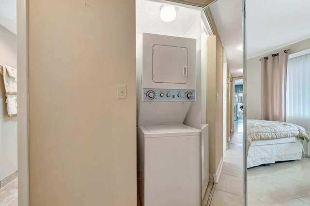 washroom featuring laundry area, light tile patterned floors, baseboards, and stacked washer / dryer