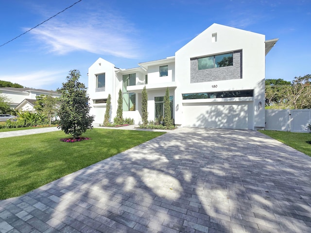 view of front of house with a front lawn, decorative driveway, a gate, and stucco siding