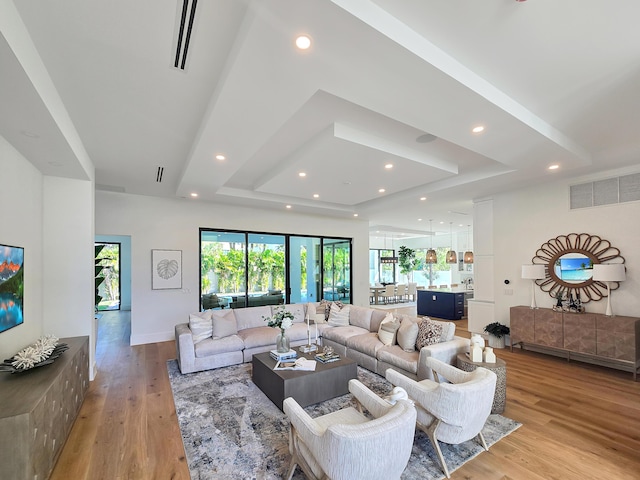 living room with light wood-type flooring, a raised ceiling, visible vents, and recessed lighting