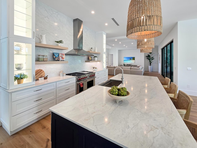 kitchen featuring range with two ovens, light stone countertops, extractor fan, open shelves, and a sink