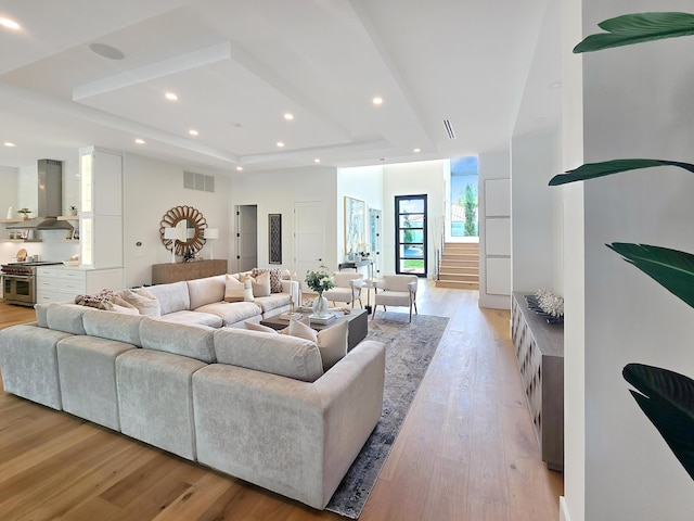 living area with a tray ceiling, light wood-style flooring, visible vents, and recessed lighting