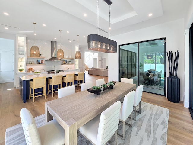 dining room featuring light wood-style floors, recessed lighting, and a raised ceiling