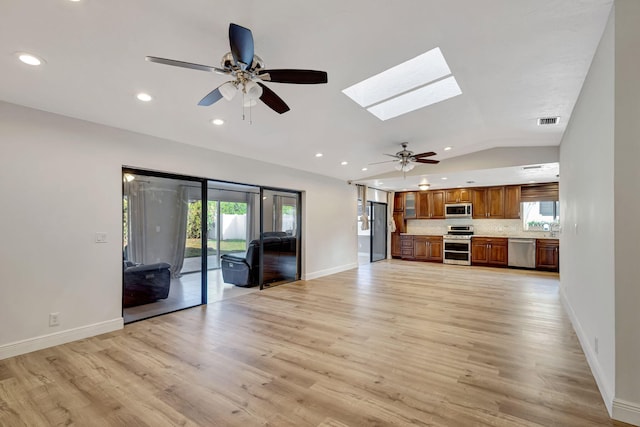 unfurnished living room featuring light wood-style floors, vaulted ceiling with skylight, a healthy amount of sunlight, and visible vents