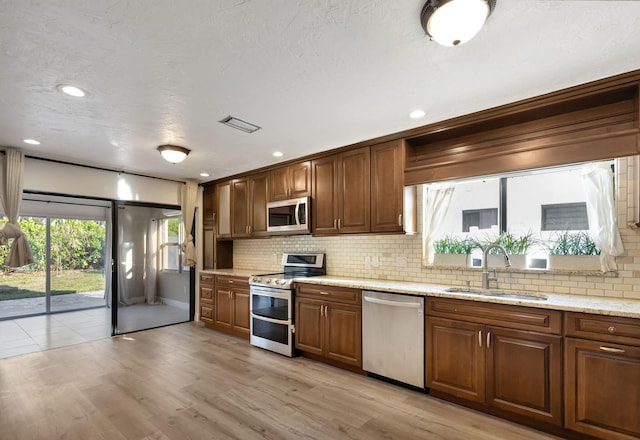 kitchen featuring light wood-style flooring, stainless steel appliances, a sink, visible vents, and decorative backsplash