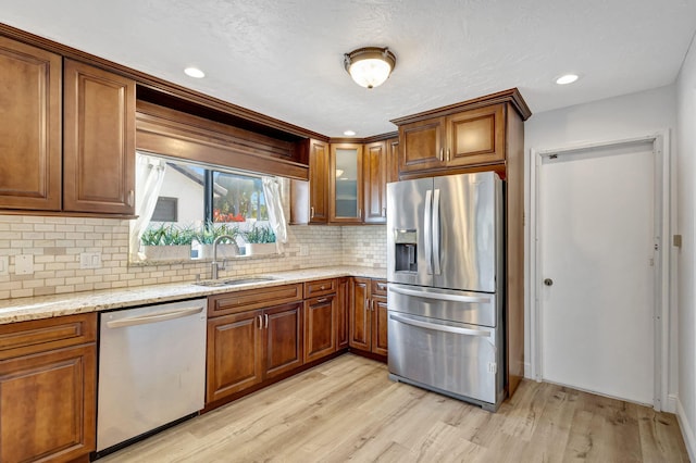 kitchen featuring light wood finished floors, light stone counters, appliances with stainless steel finishes, brown cabinets, and a sink