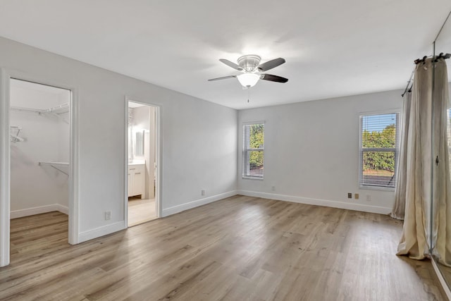 unfurnished bedroom with a walk in closet, light wood-style flooring, and baseboards