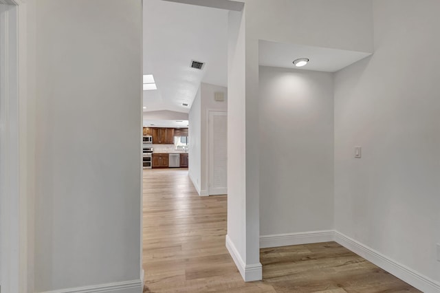 hall with lofted ceiling, light wood finished floors, visible vents, and baseboards