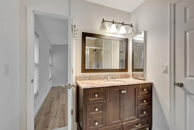 bathroom with a shower with door, wood finished floors, vanity, and baseboards