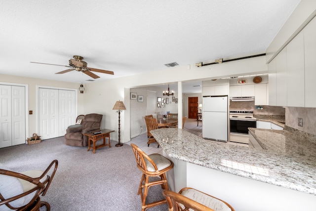 kitchen with white appliances, visible vents, a peninsula, extractor fan, and white cabinetry