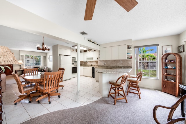 dining space with light tile patterned floors, a textured ceiling, light colored carpet, ceiling fan with notable chandelier, and visible vents