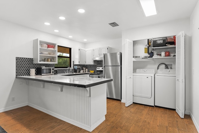 kitchen featuring washing machine and dryer, a peninsula, white cabinets, appliances with stainless steel finishes, and dark wood-style floors