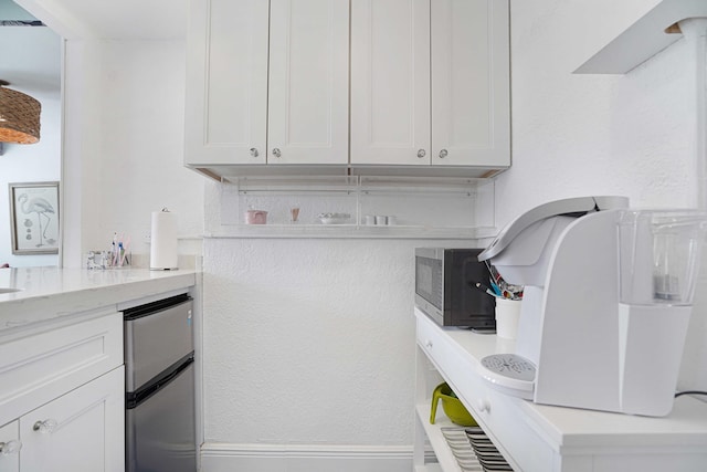 kitchen with light stone countertops, baseboards, white cabinetry, and stainless steel microwave