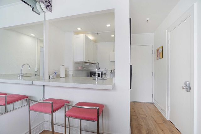 kitchen featuring a breakfast bar area, a sink, light wood-style floors, white cabinets, and light countertops