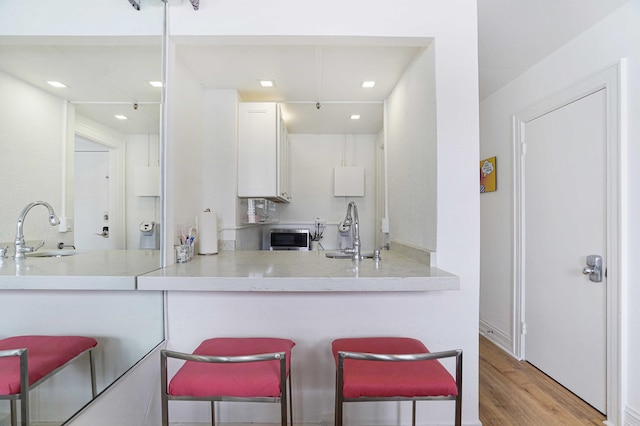 235 Sunrise Ave Unit 3225, Palm Beach, FL 33480 - kitchen featuring white cabinetry, wood finished floors, a kitchen breakfast bar, recessed lighting, and light countertops