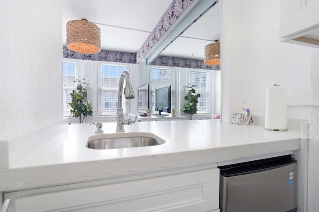 kitchen featuring a textured wall, white cabinets, a sink, and freestanding refrigerator