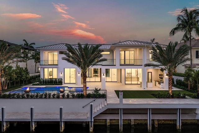 191 W Coconut Palm Rd, Boca Raton, FL 33432 - back of house at dusk with a standing seam roof, stucco siding, a patio, an outdoor pool, and metal roof