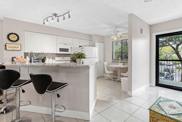 kitchen featuring light stone counters, a peninsula, white appliances, white cabinetry, and decorative backsplash