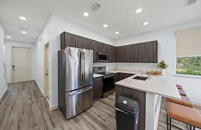 kitchen featuring a breakfast bar area, a peninsula, stainless steel appliances, light countertops, and a sink