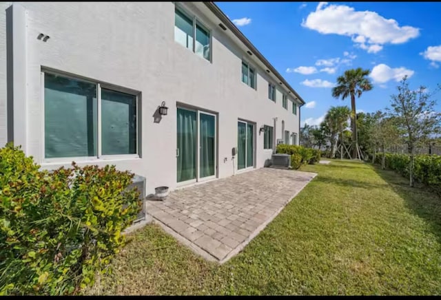 rear view of property featuring a yard, central air condition unit, a patio, and stucco siding