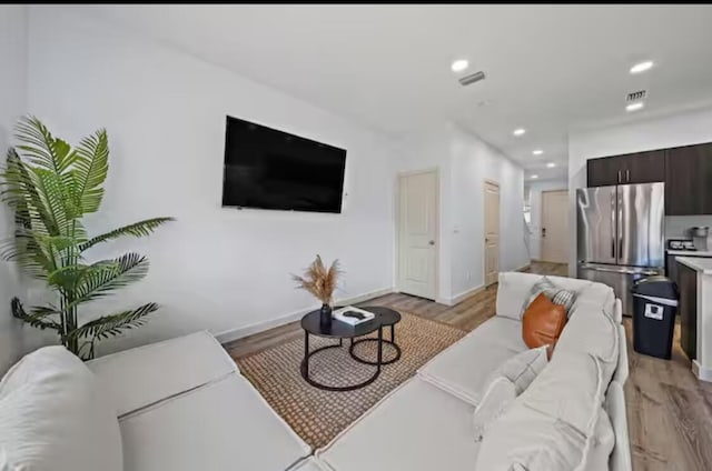 living area featuring baseboards, light wood finished floors, visible vents, and recessed lighting